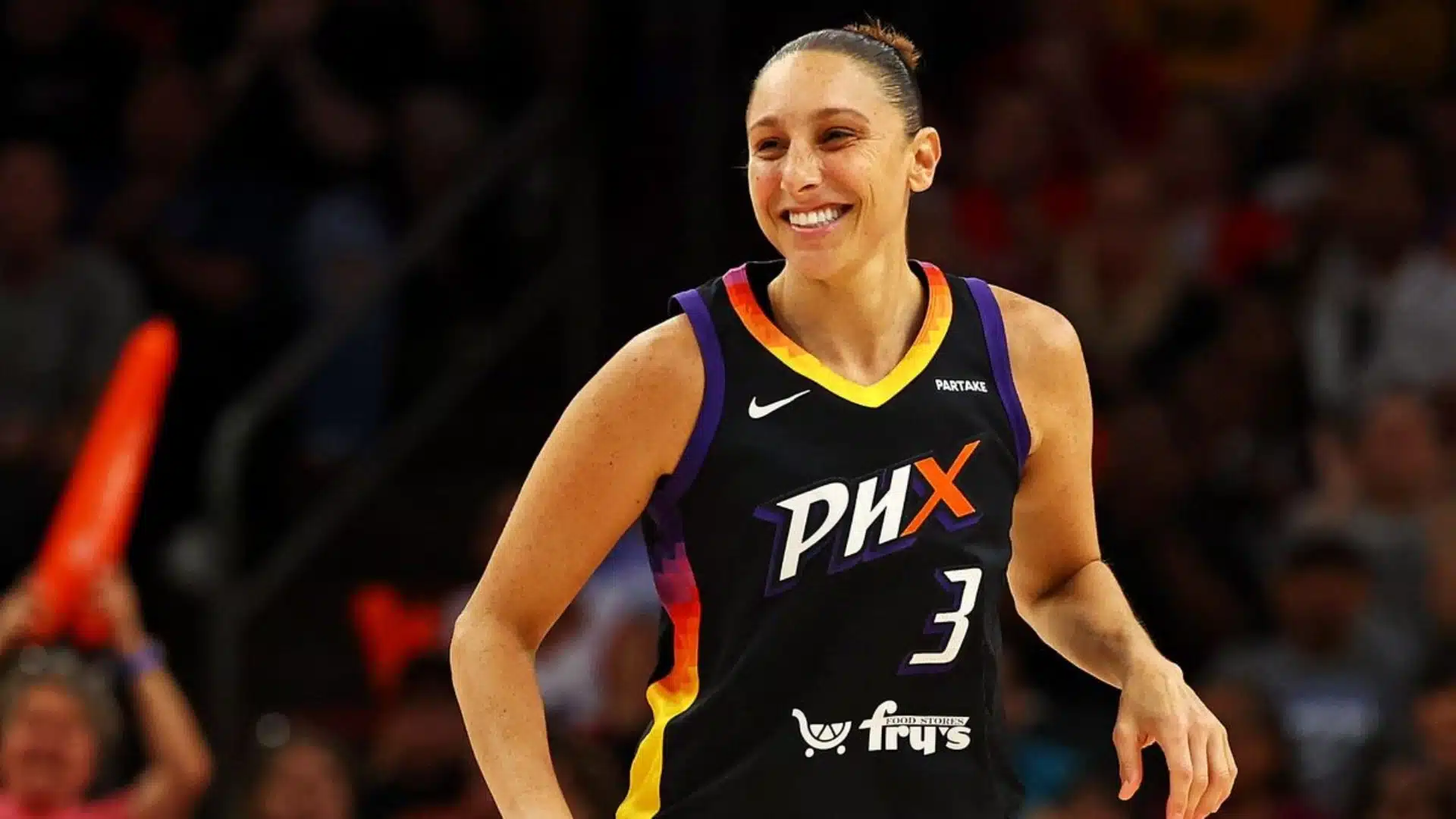 Basketball player smiling on the court while wearing a Phoenix team uniform during a game.