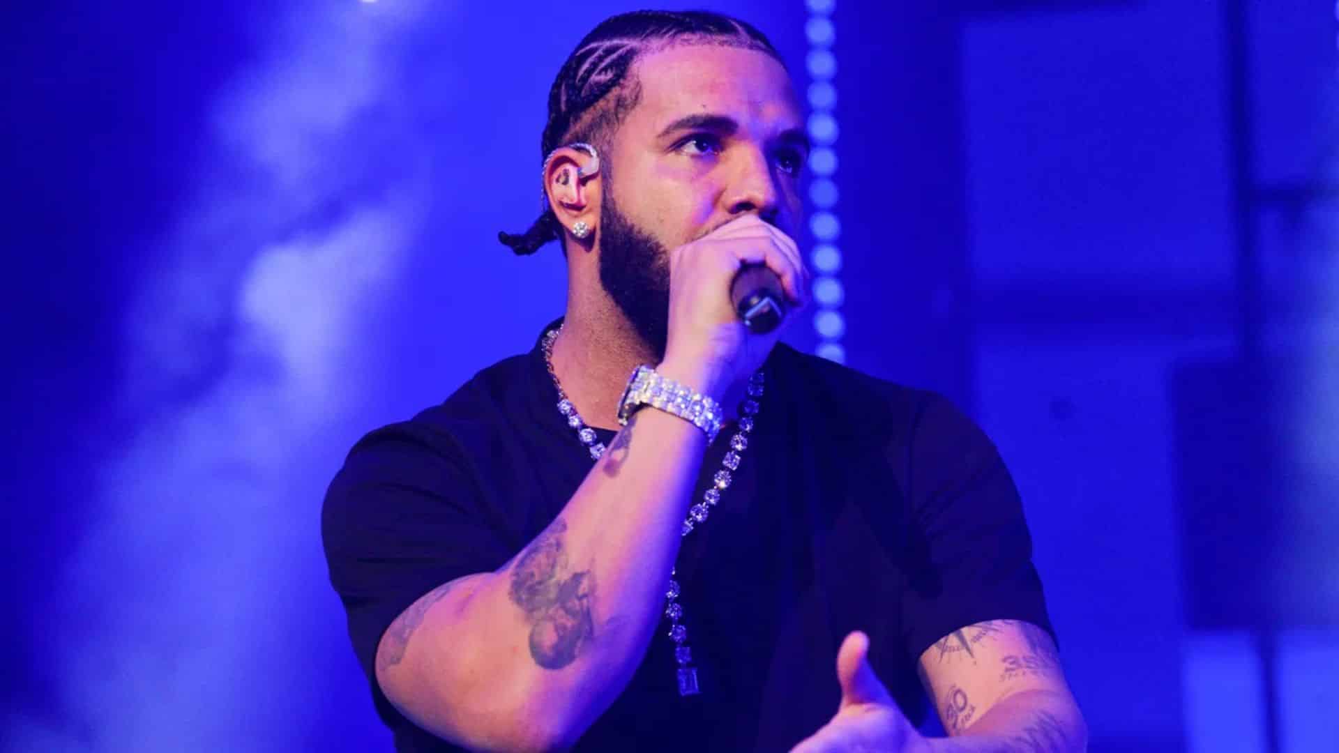 Drake performing on stage during a concert, holding a microphone and singing under blue stage lighting with focused expression