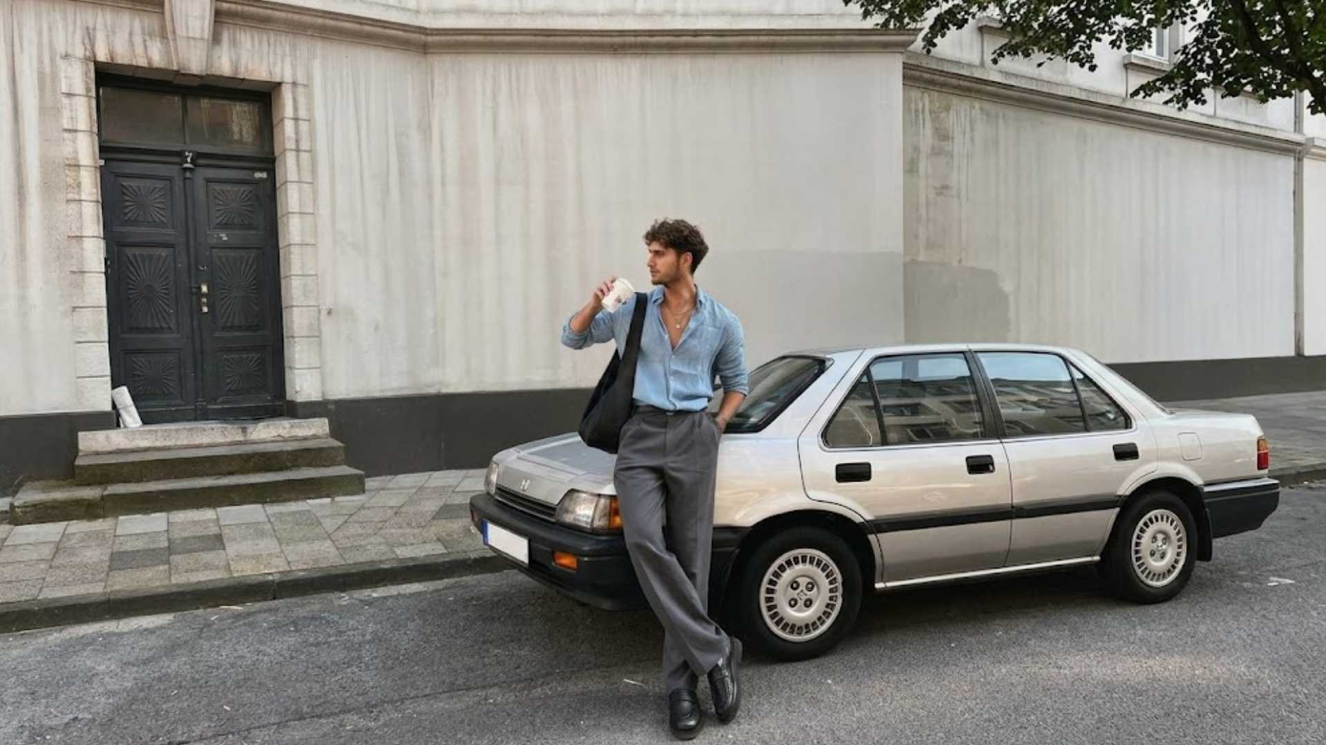 Man wearing a drinks after work outfit with blue button down shirt gray trousers and leather shoes beside a car