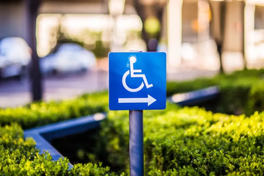 Blue wheelchair accessibility sign with right arrow among green hedges outdoors