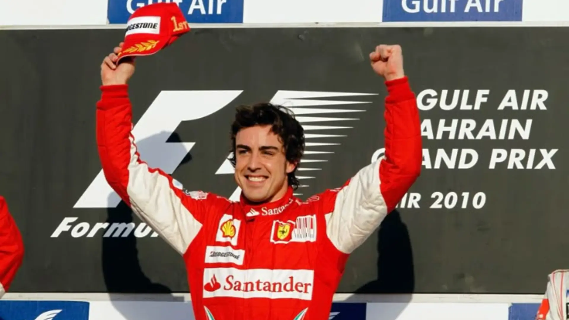 Formula One driver celebrating on the podium in a red racing suit with arms raised in victory.