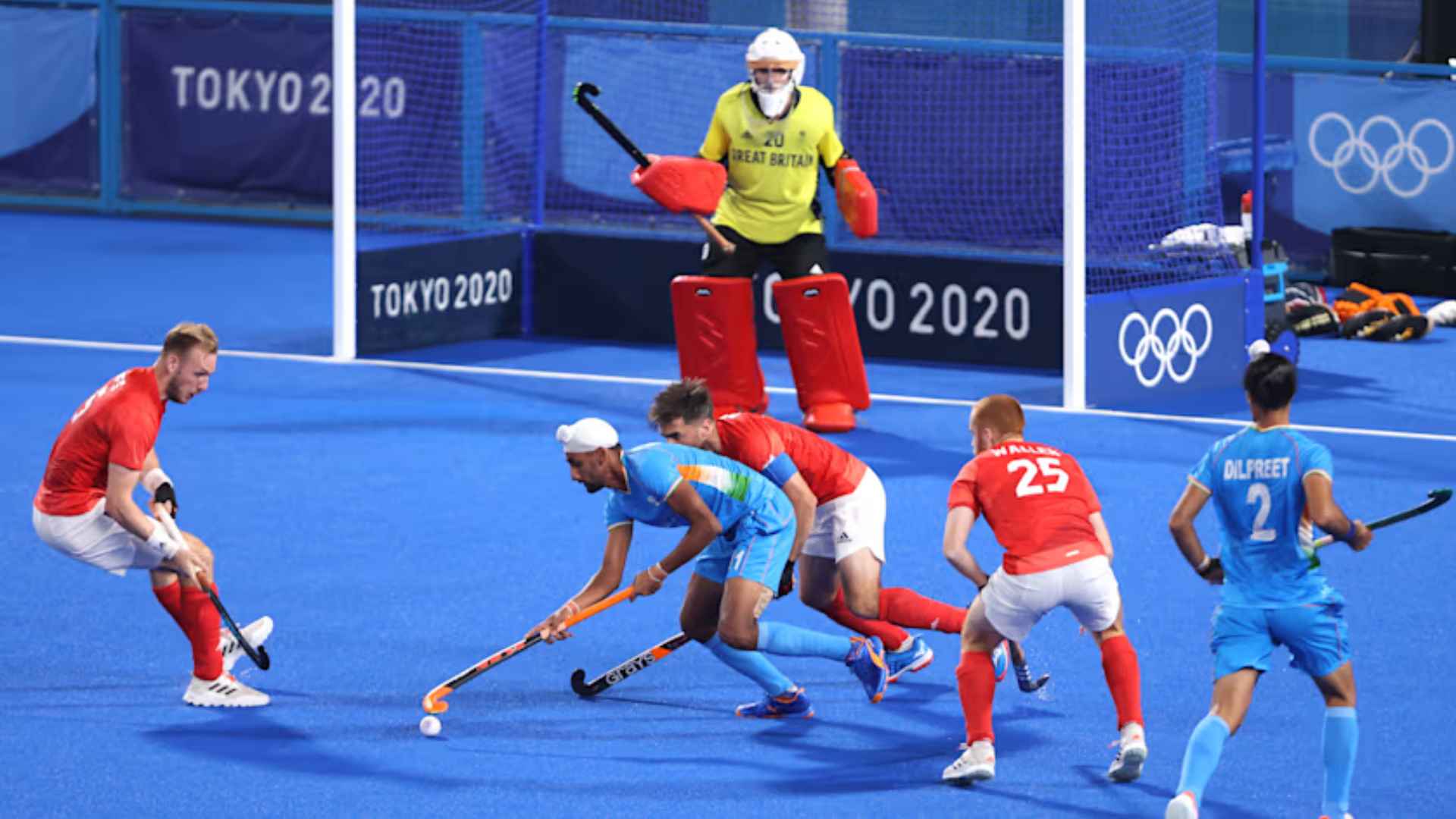 Field hockey players battle for the ball near the goal during an Olympic match on a blue artificial turf field.
