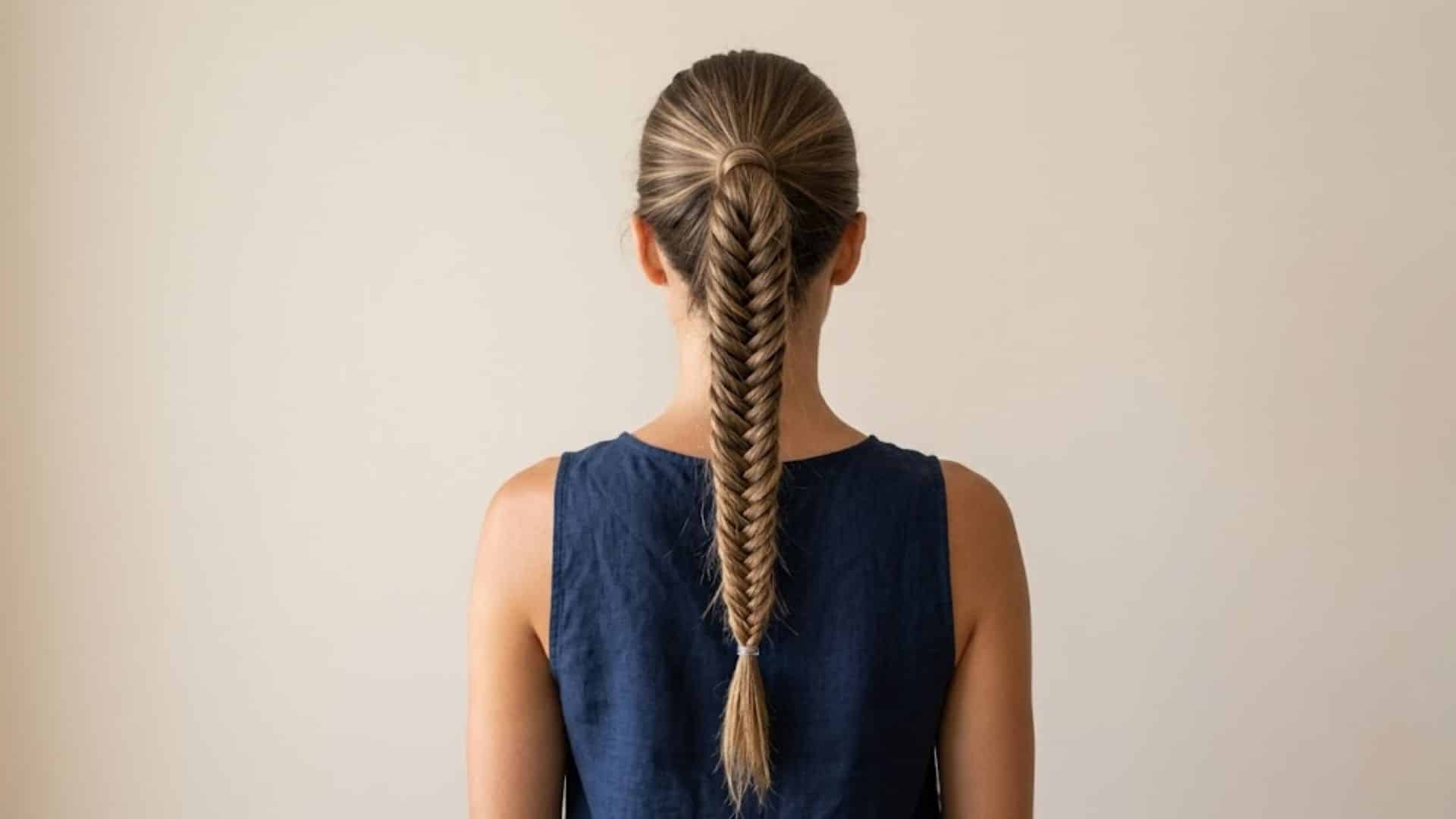 A detailed fishtail ponytail braid centered on a woman's back against a plain wall.