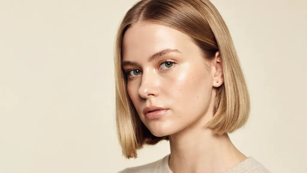 Woman showcasing a sleek blonde bob haircut with a center part and smooth styling in a minimalist beauty portrait