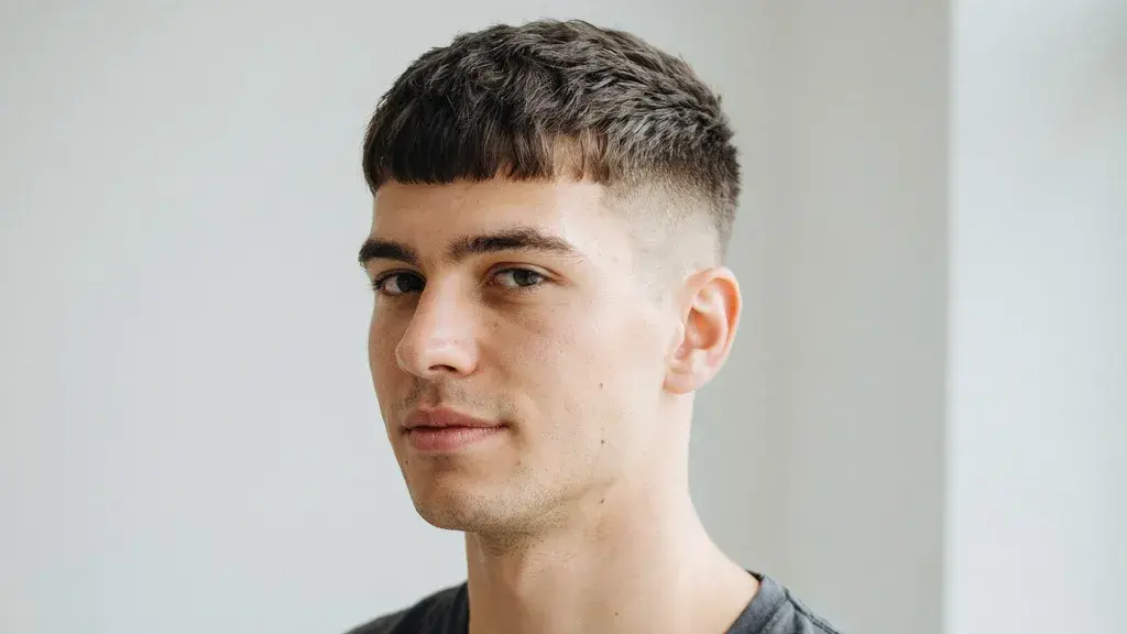 Man showcasing a modern textured haircut with a clean fade, short fringe, and natural styling in a minimal indoor setting