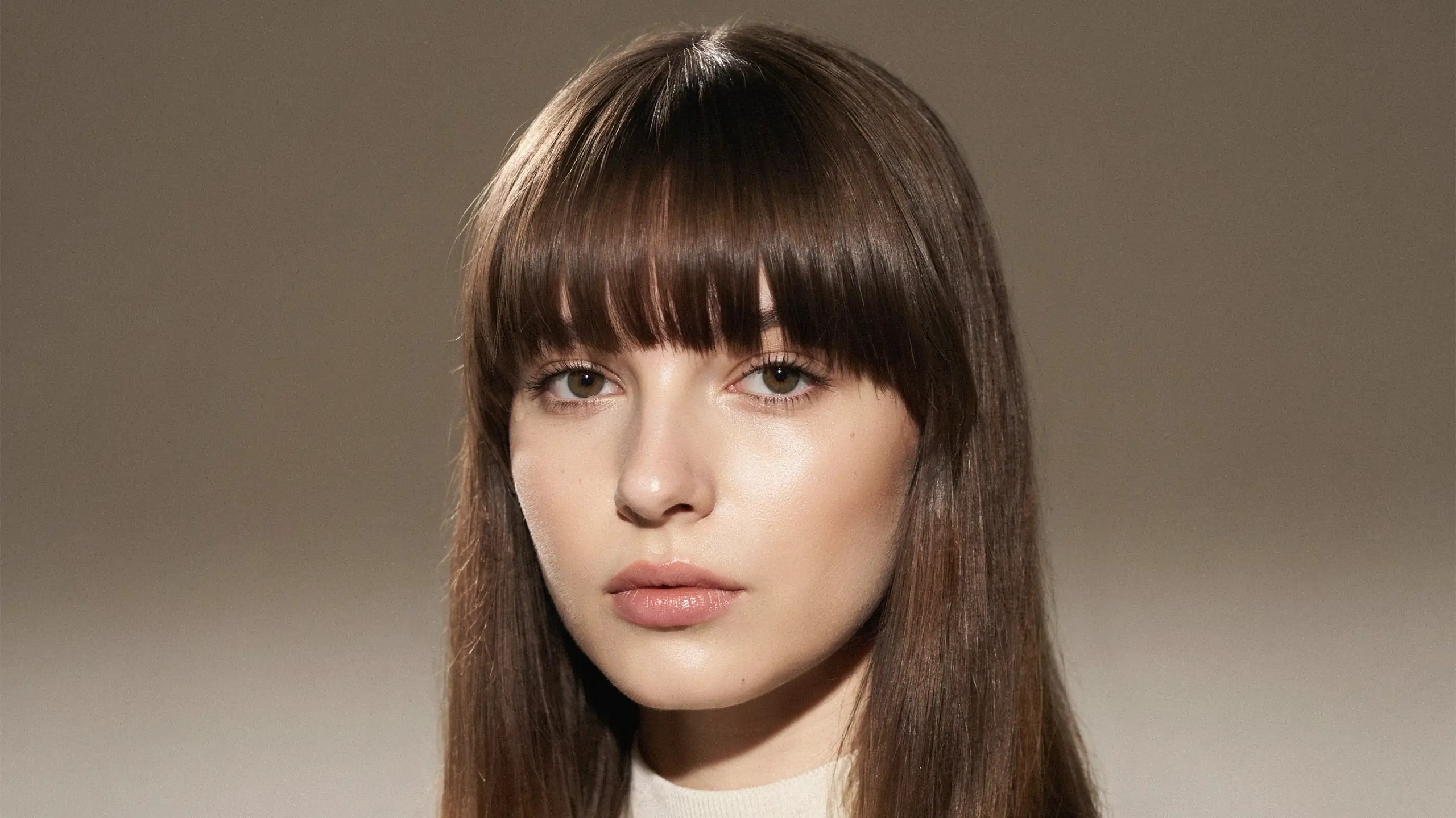 Heavy full bangs covering the forehead with sleek straight hair and bold framing
