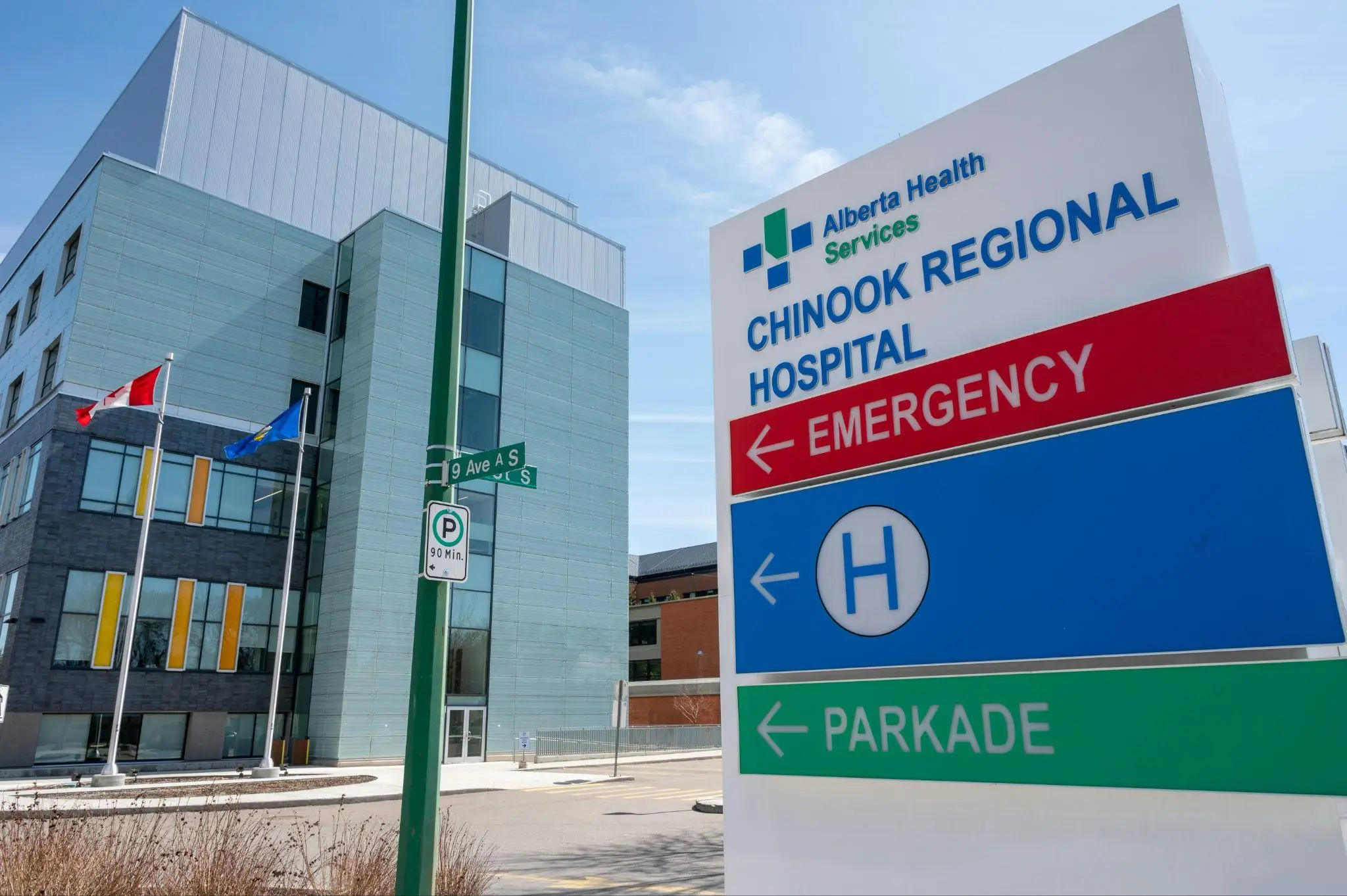 Hospital signage with emergency and parking directions, building and flags in the background