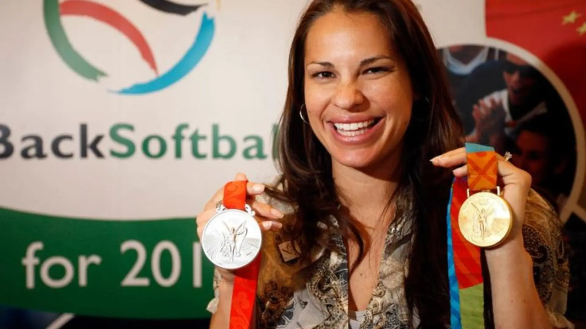 Smiling woman holds up a silver and gold medal at a Back Softball event.