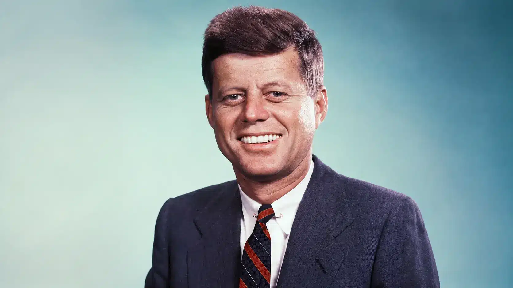 John f kennedy in dark suit and striped tie posed against soft blue gradient studio background portrait