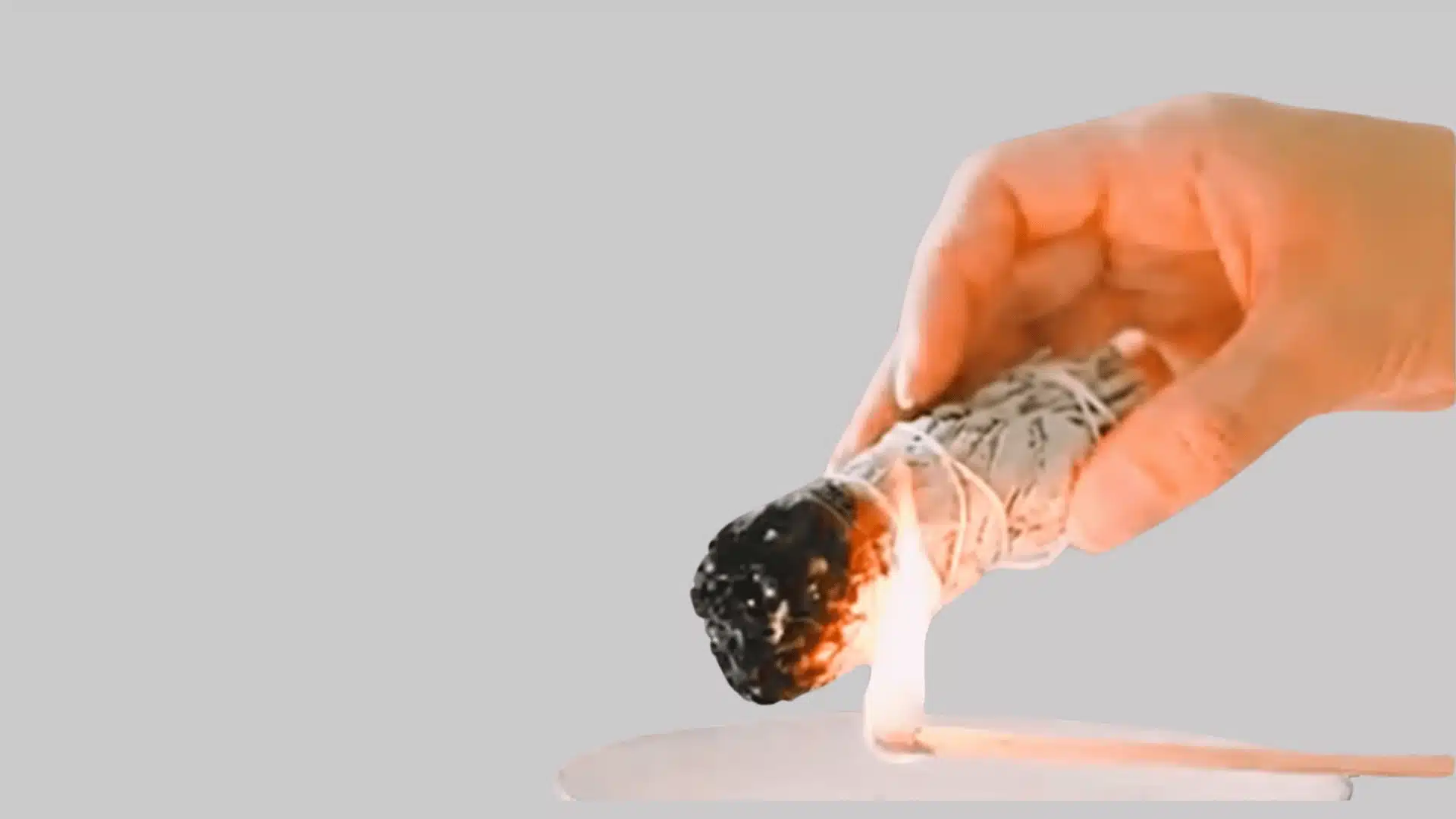 Hand lighting a sage bundle over a fire-safe bowl during smudging