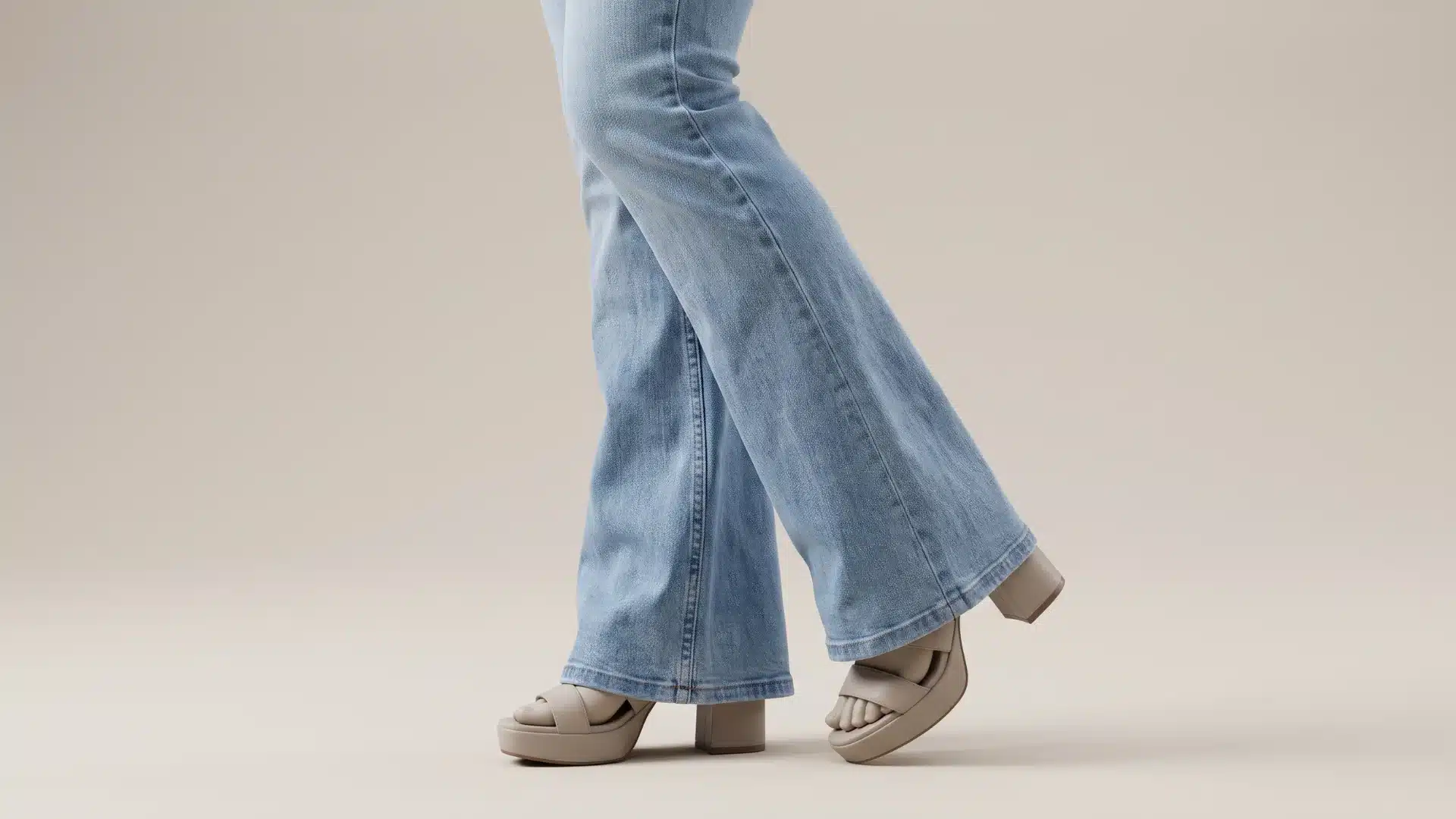 Close up view of light wash flare jeans showing wide leg openings paired with beige platform heels in a studio setting