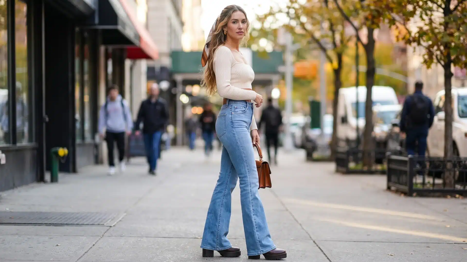 Woman wearing light wash flare jeans with a white sweater and heels while walking through a city street fashion setting