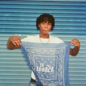 Lil Loaded holding a blue bandana in front of a corrugated metal shutter while smoking.