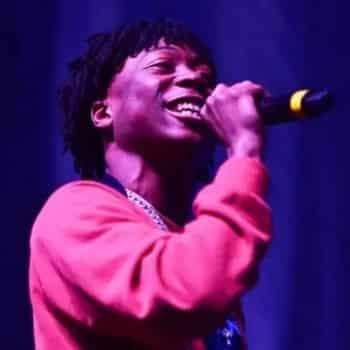 Lil Loaded performing on stage, singing into a microphone under purple stage lighting.