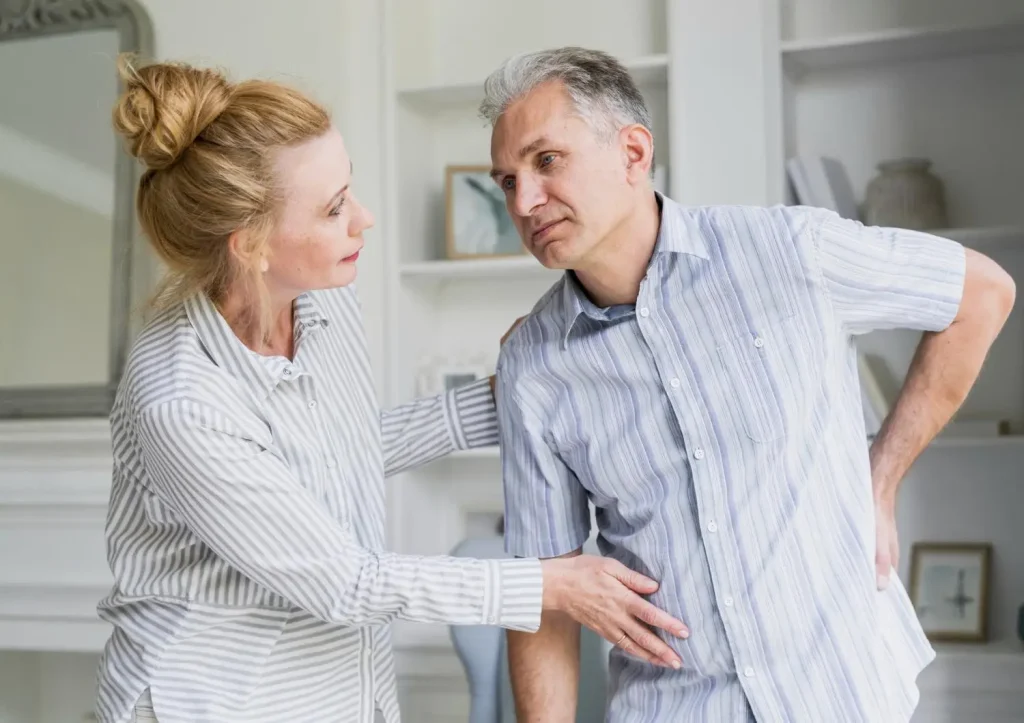 Woman supporting man with back pain in a bright living room setting