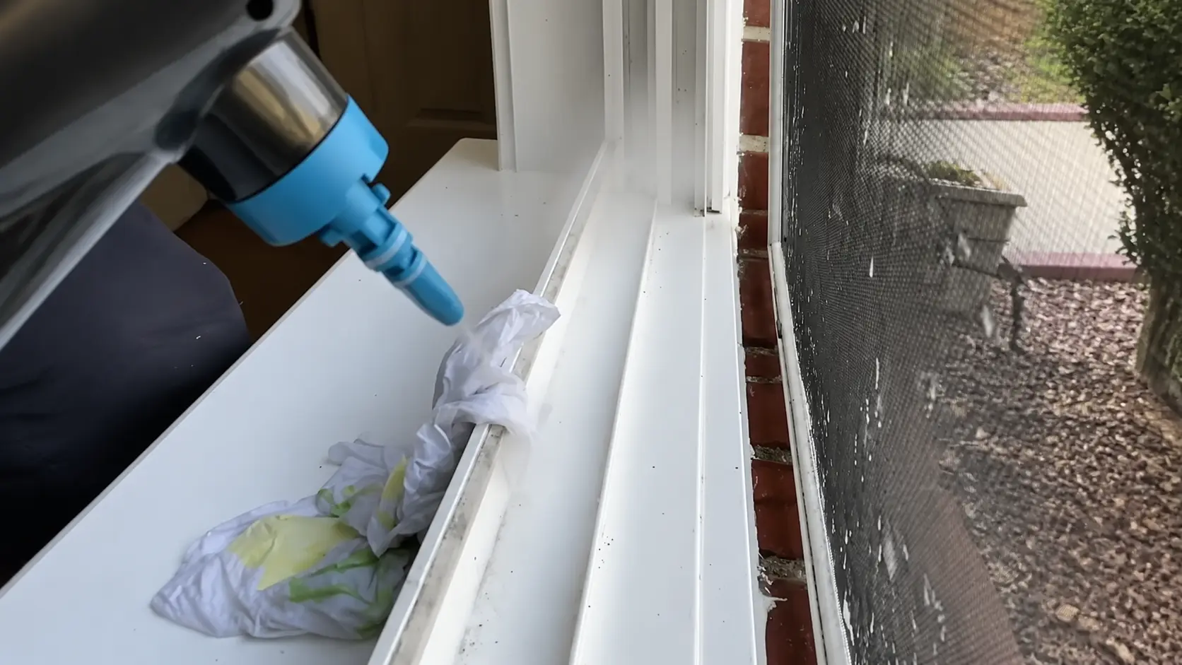 handheld steamer cleaning a window track with a cloth nearby, removing dirt from the window sill