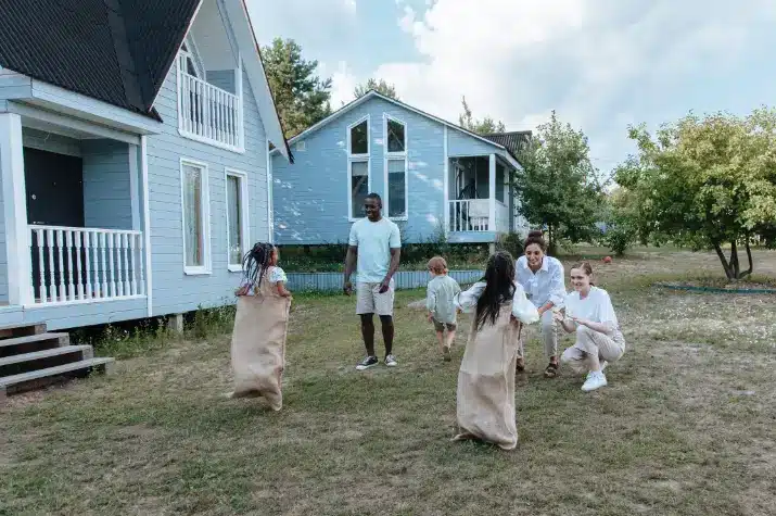 Children having a sack race on grass lawn near blue houses under cloudy sky