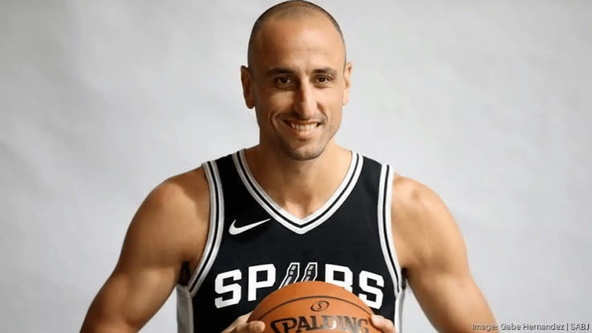 Basketball player wearing a Spurs jersey holding a basketball in a studio setting