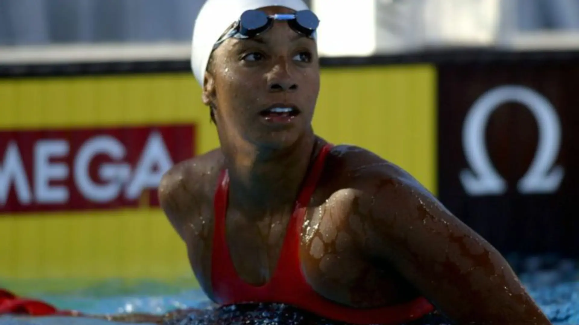 Swimmer wearing goggles and a cap emerges from the pool during a competitive race.