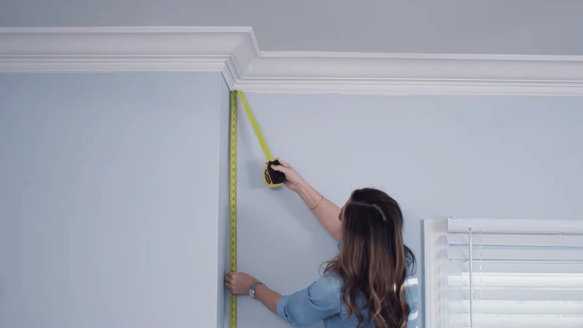 Person measuring a wall corner with a tape measure during home renovation work