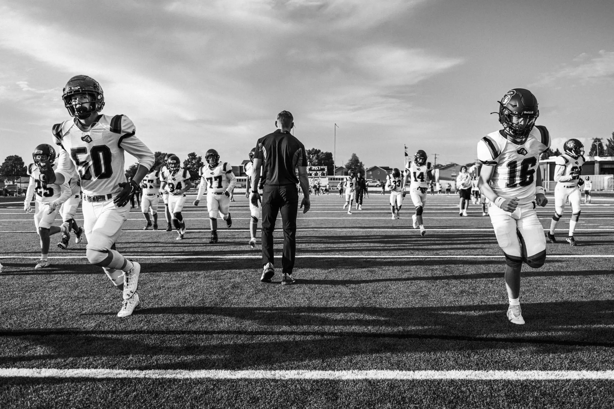 Football players and coach on field during practice in black and white scene