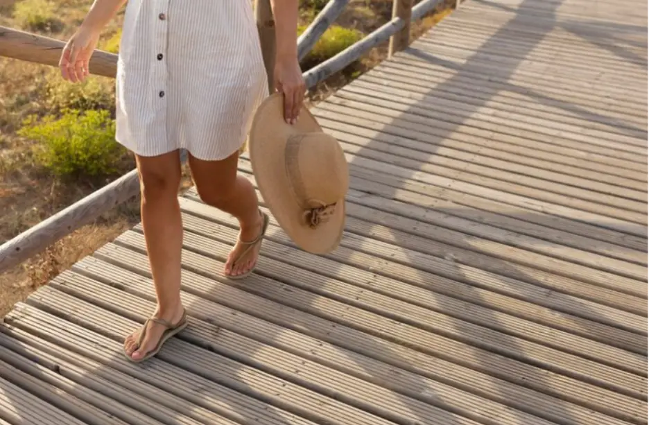 Person walking on wooden boardwalk holding straw hat in sunny outdoor setting