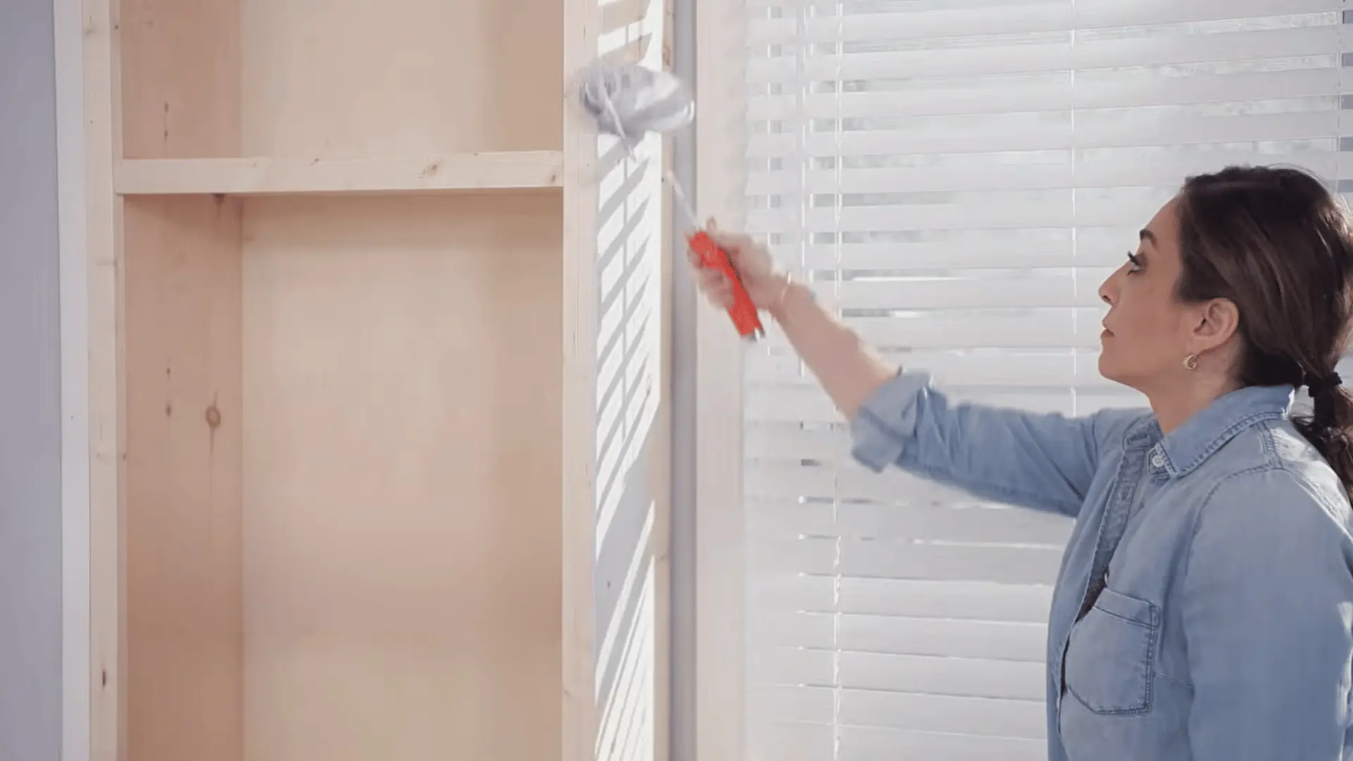 Person applying finish to a wooden shelving unit with a brush during a DIY project
