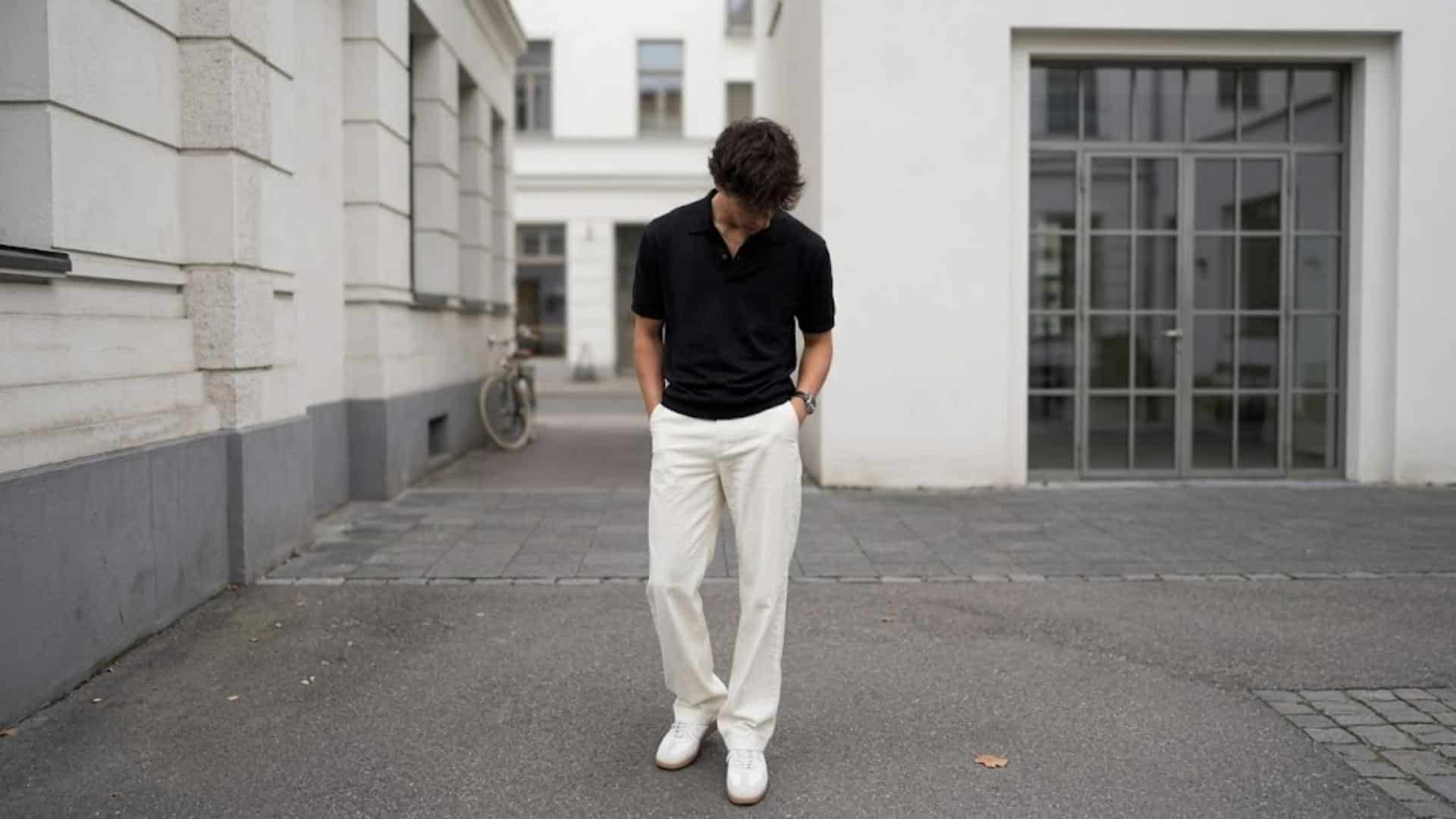 Man wearing a black polo shirt with white trousers and sneakers in a clean smart casual date outfit