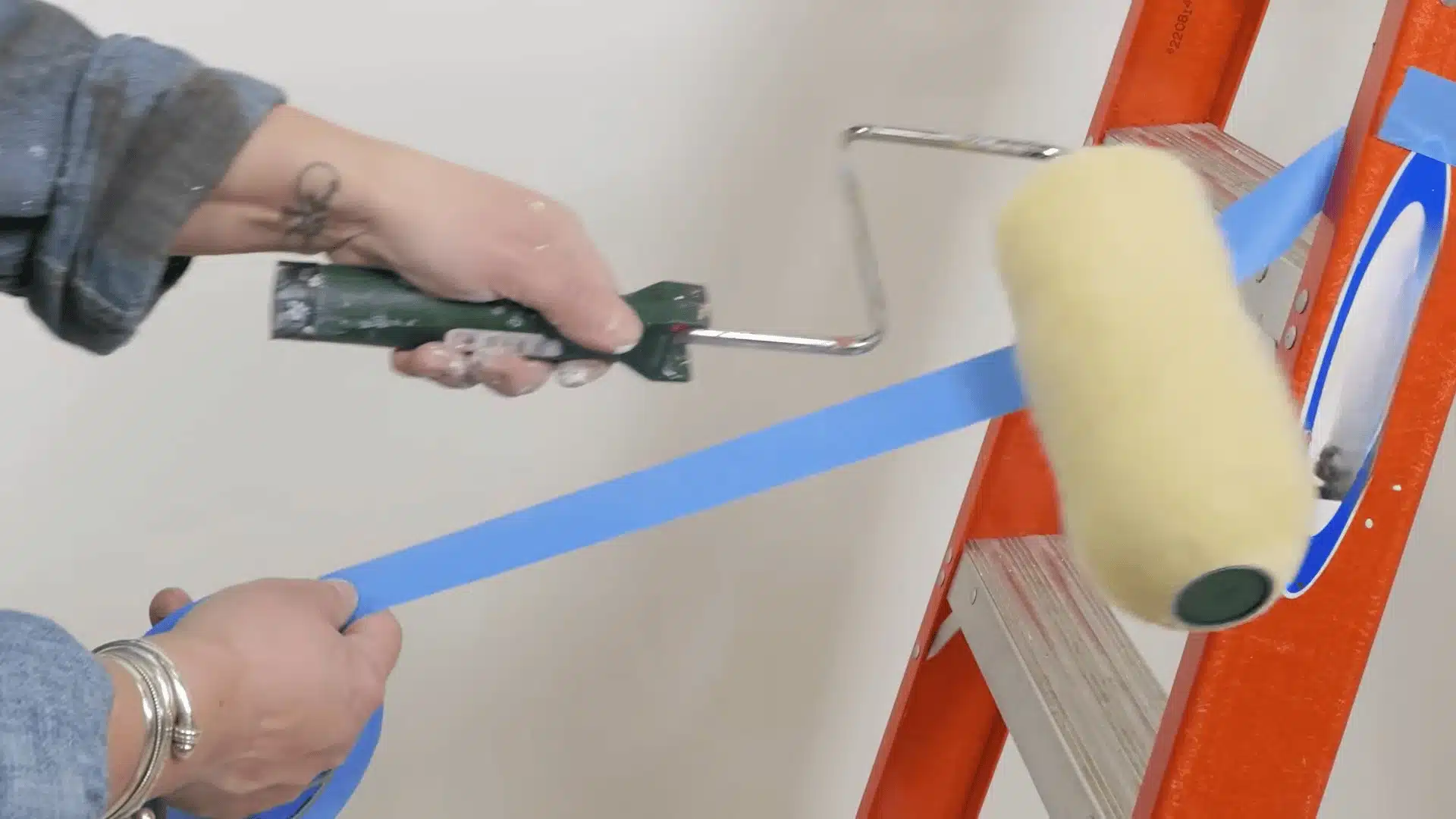 Painter preparing a roller and applying painter’s tape before painting a popcorn ceiling.