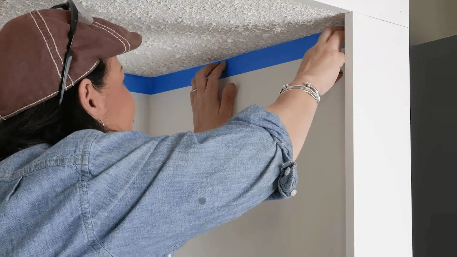 Person applying painter’s tape along wall edges to protect surfaces before painting a popcorn ceiling.