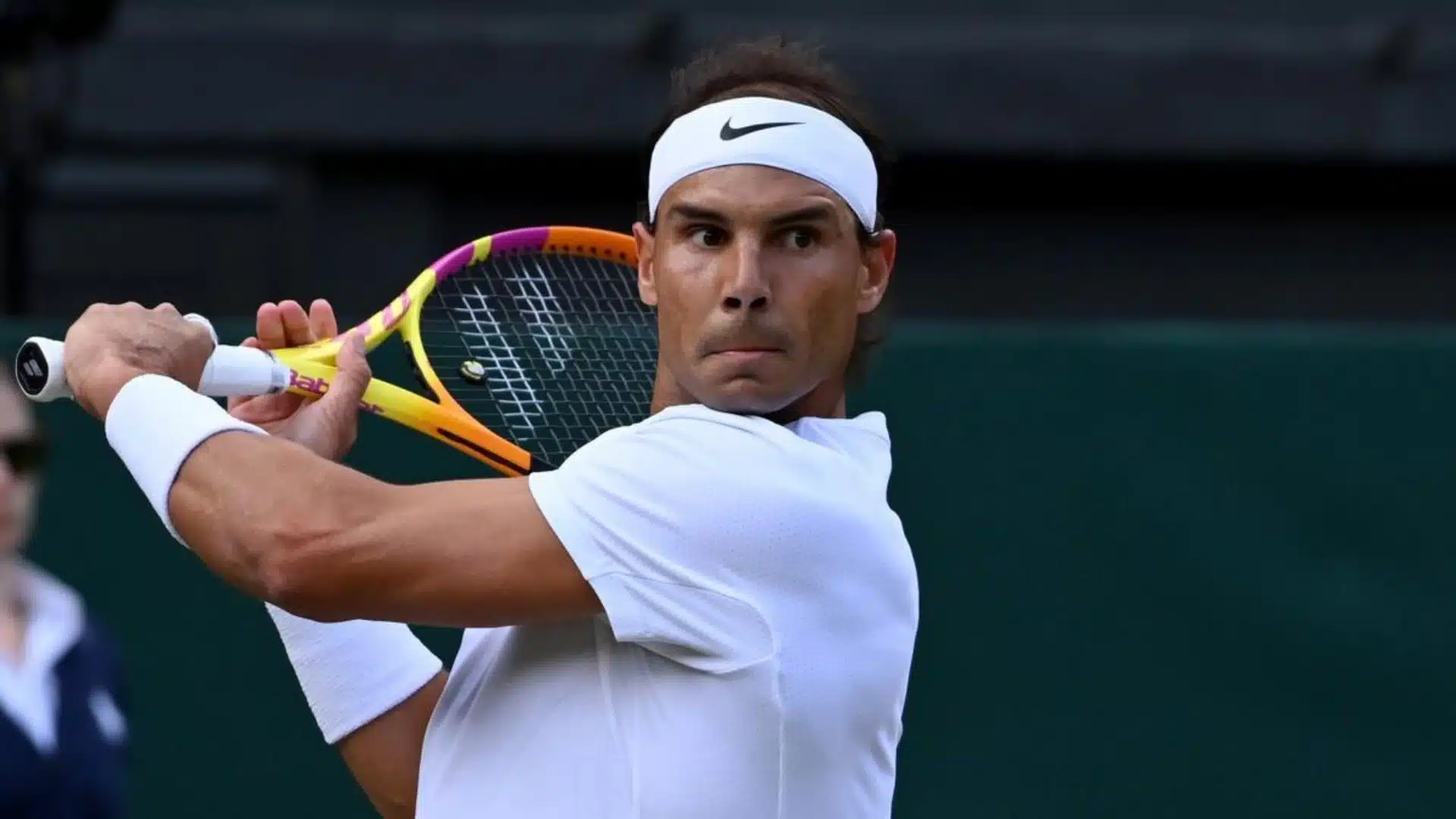 Tennis player preparing a backhand shot while wearing a white outfit on the court.