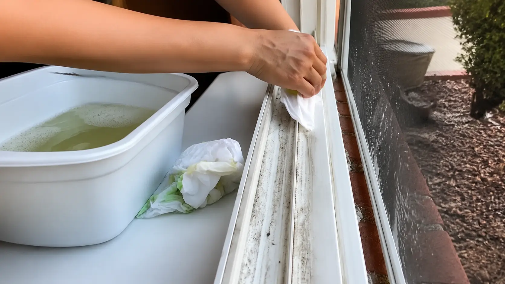 person cleaning a dirty window track with a cloth, removing dust and grime from the groove
