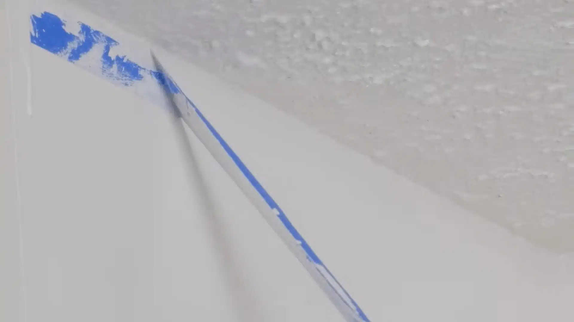 Painter’s tape being removed from a clean ceiling edge after painting a popcorn ceiling.