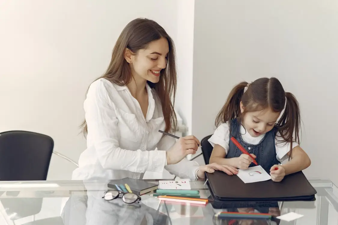 Woman and child drawing together at glass desk in bright room