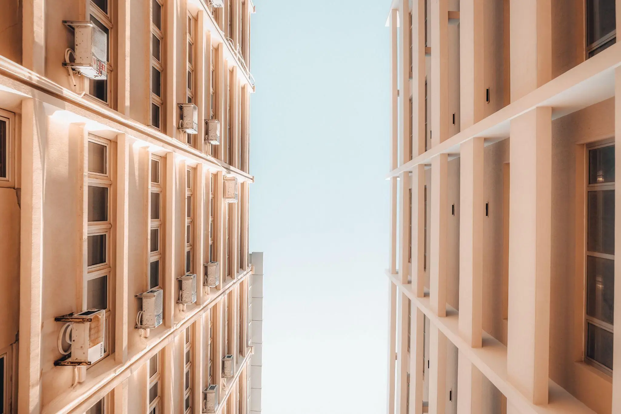 Tall modern buildings with rows of windows and air conditioners against blue sky