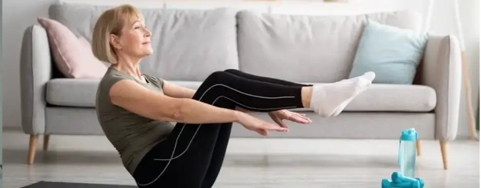 Older woman practicing yoga poses on mat in living room with dumbbells nearby