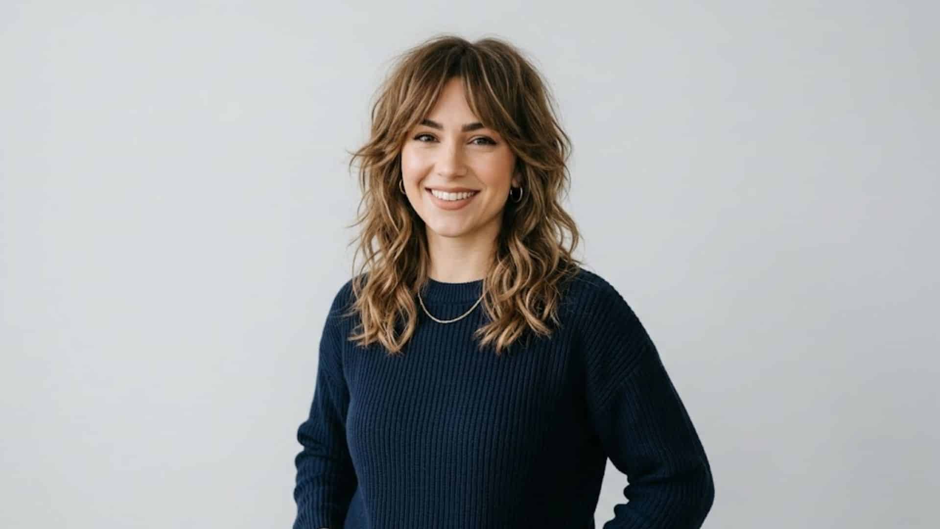 Woman with a wavy shoulder-length shag haircut, curtain bangs, and balayage highlights smiling