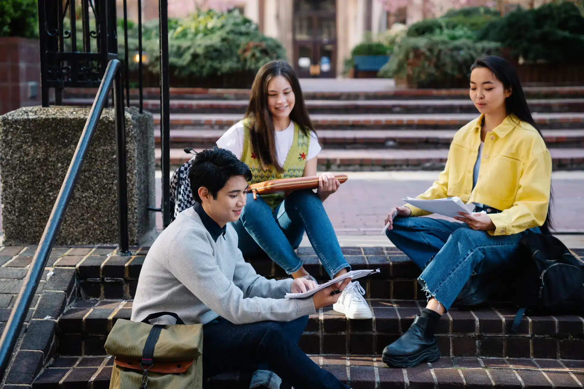 Three students studying on brick steps outdoors with notebooks and backpacks