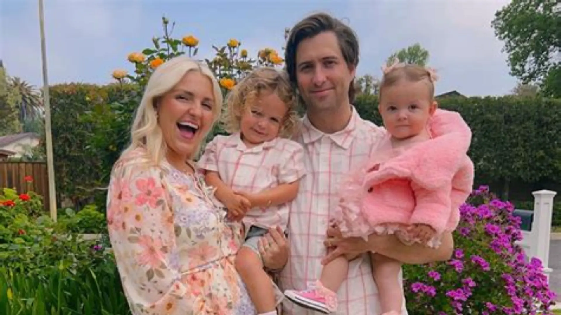 Family outdoor portrait showing two adults with children standing together in a garden setting on a bright day