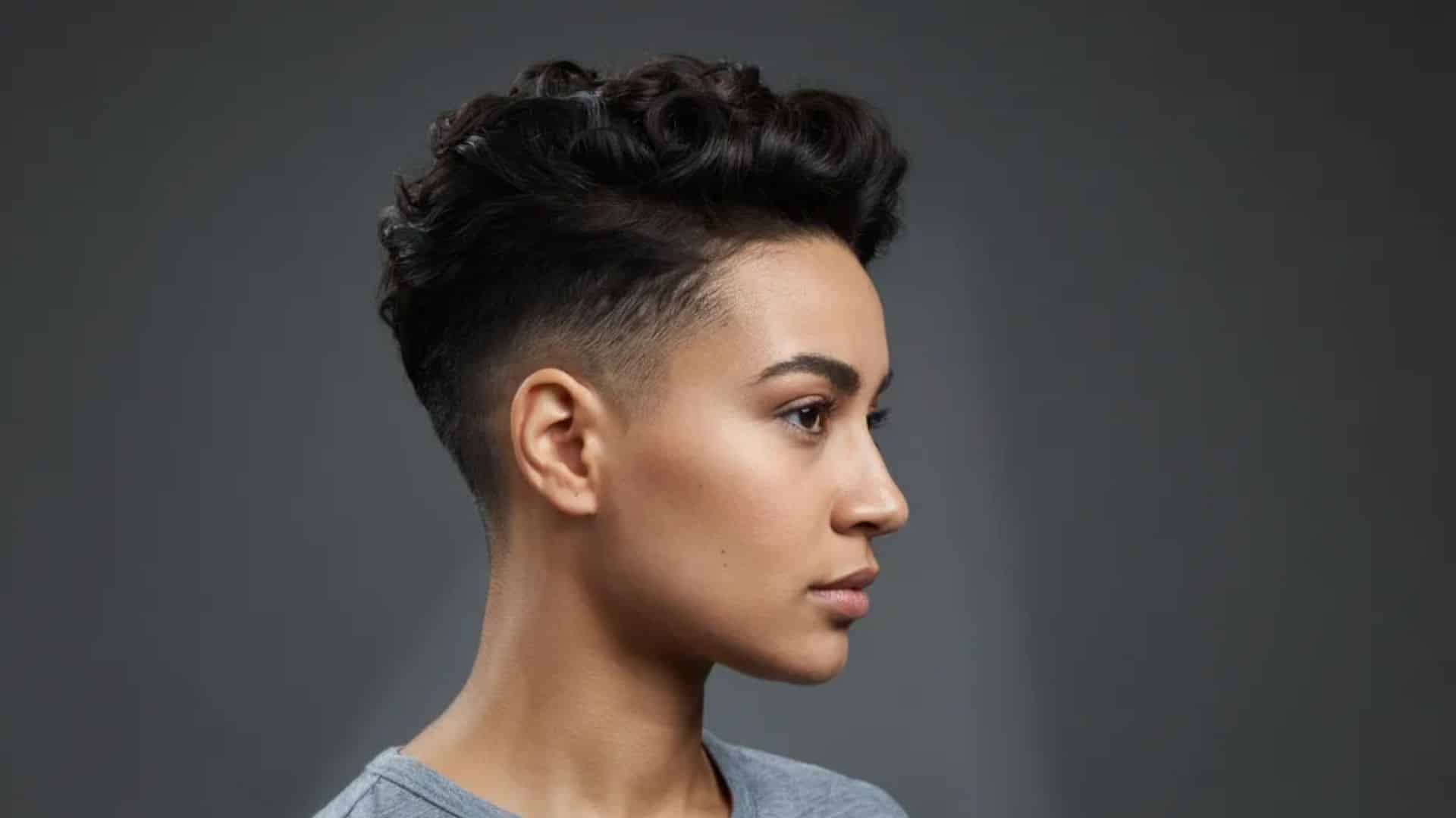 Curly taper fade pixie with voluminous curls on top, closely shaved sides.
