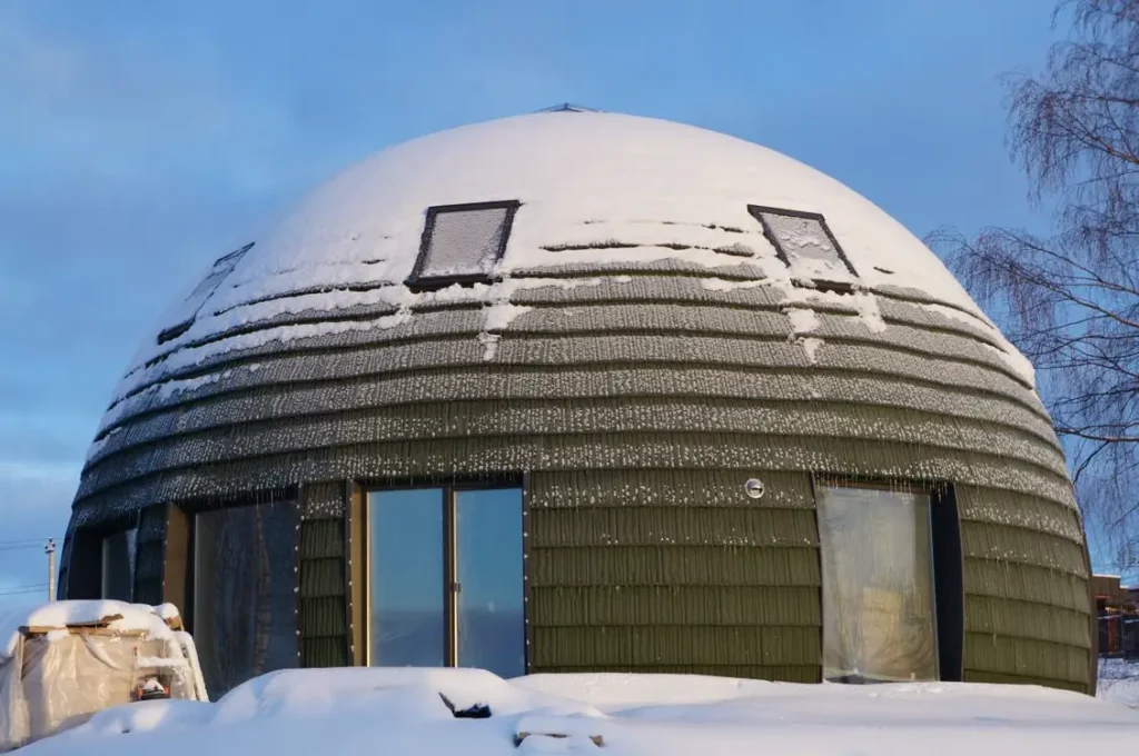 Dome-shaped house covered in snow with frosted windows under a blue sky