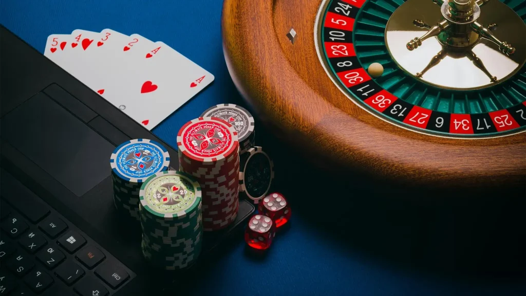 Roulette wheel next to poker chips and cards on blue casino table