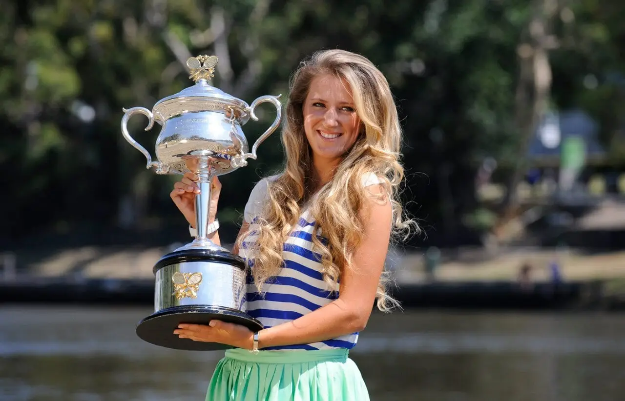 Person with long hair holding a large silver trophy outdoors with blurred trees in background