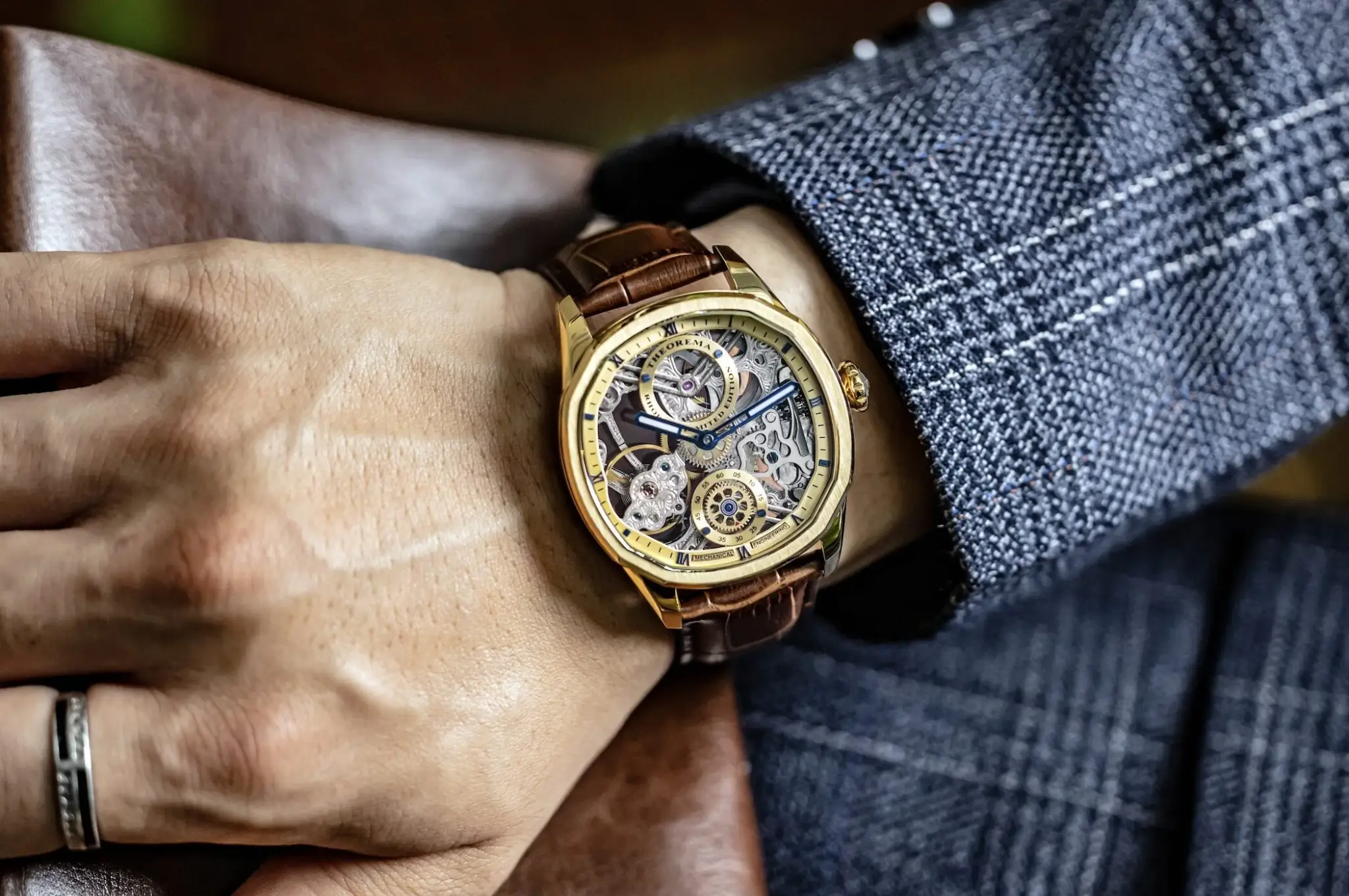 Gold skeleton watch with brown leather strap on wrist wearing tweed jacket