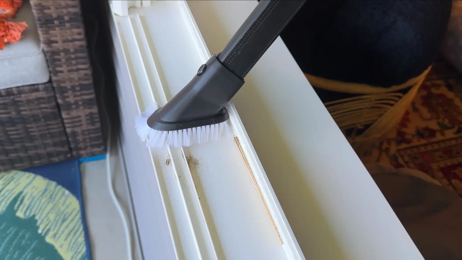 a vacuum brush attachment running along a dirty white window track, picking up loose debris from the channels