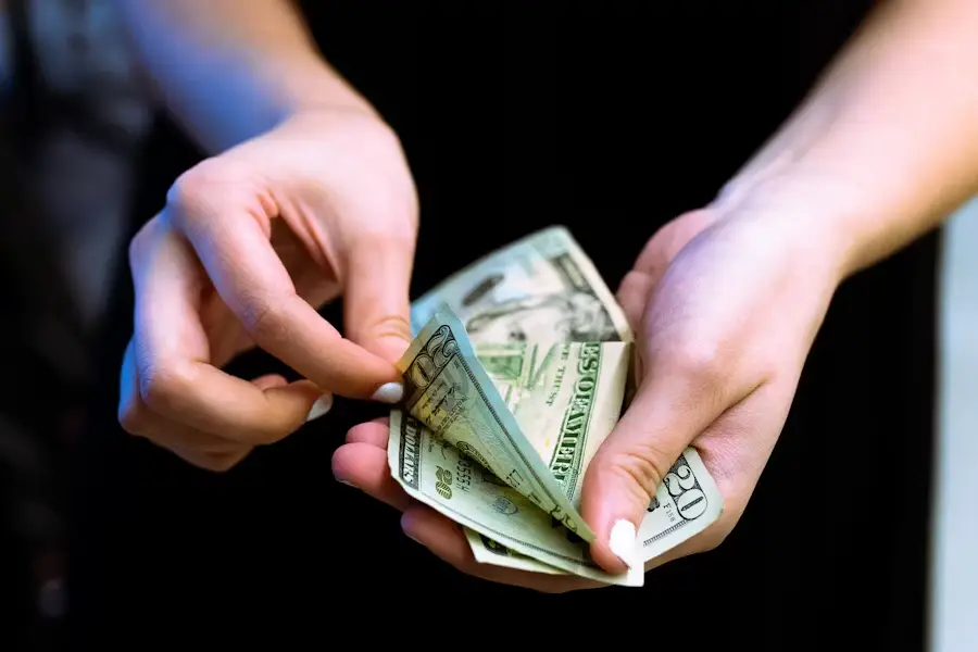 Hands counting US dollar bills against dark background