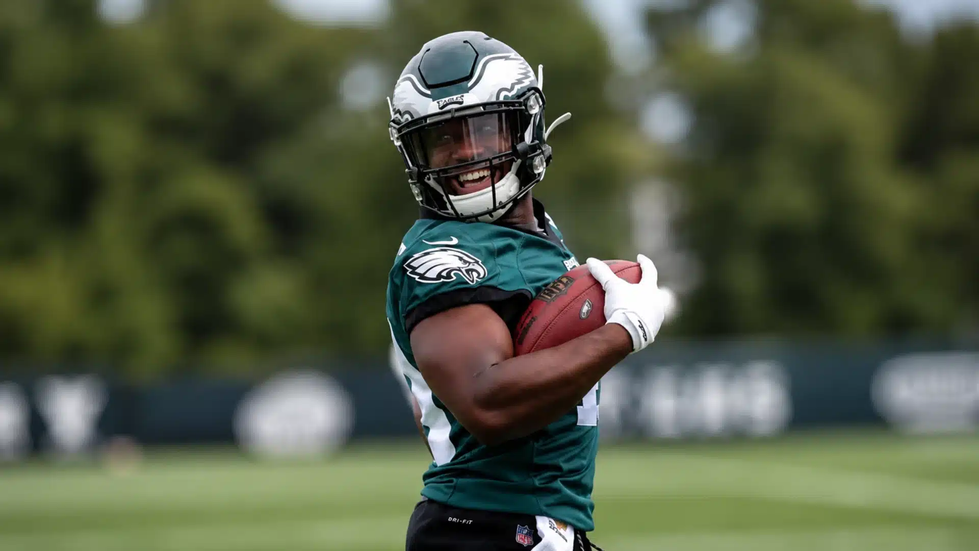 Boston Scott wearing a helmet and holding a football during practice on a field.