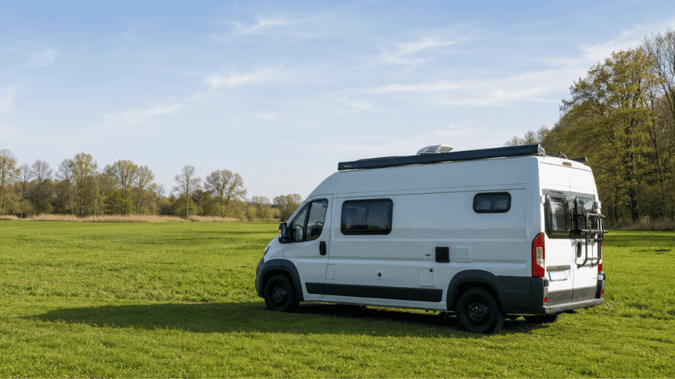 White travel van parked in a wide green field under a clear blue sky