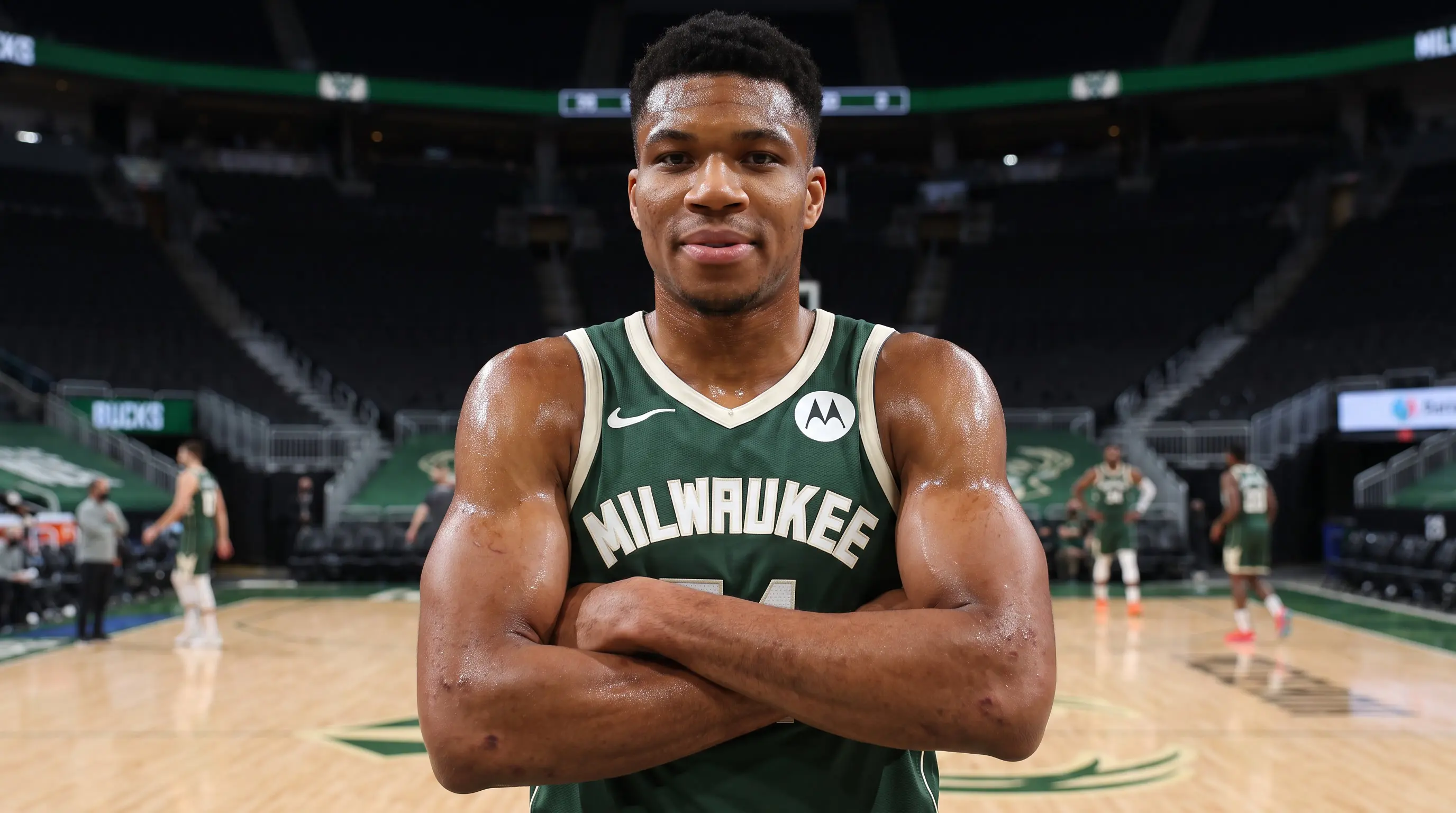 Giannis Antetokounmpo poses with folded arms on the Milwaukee Bucks court before an NBA game.