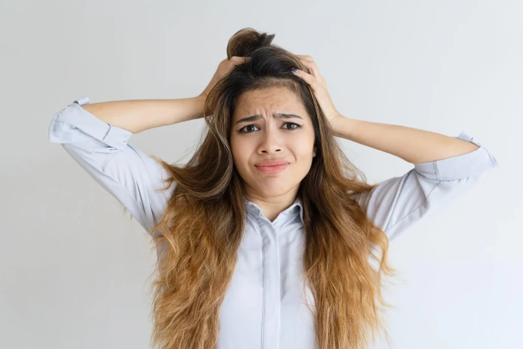 Woman with long hair looking frustrated, pulling at her head indoors